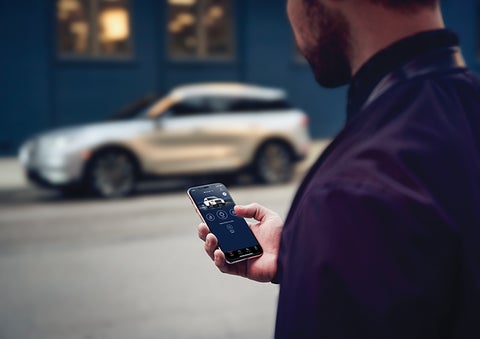 A person is shown interacting with a smartphone to connect to a Lincoln vehicle across the street. | Dave Sinclair Lincoln in St Louis MO