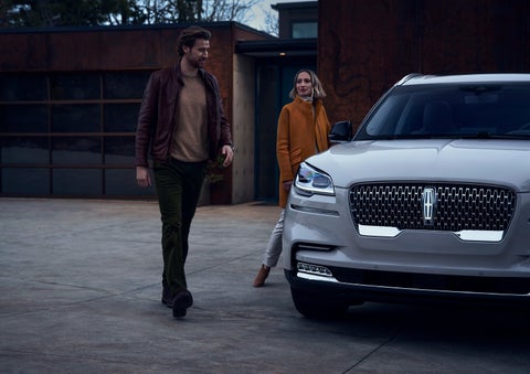 A man and a woman approaching a 2024 Lincoln Aviator® SUV, which illuminates certain lights when they are close | Dave Sinclair Lincoln in St Louis MO